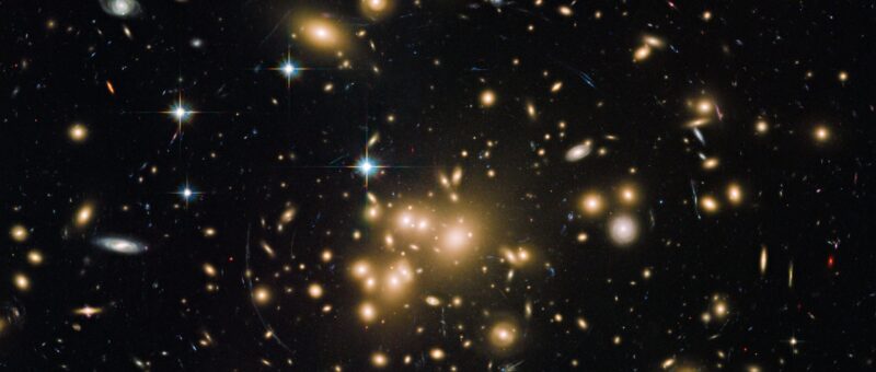 A cluster of yellow galaxies and white stars appear on a black background.