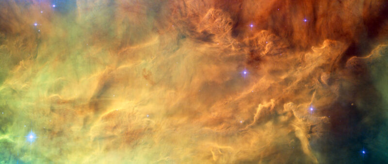 Waves of interstellar gas and dust, ranging in color from green to yellow to orange, mix in the Lagoon Nebula.