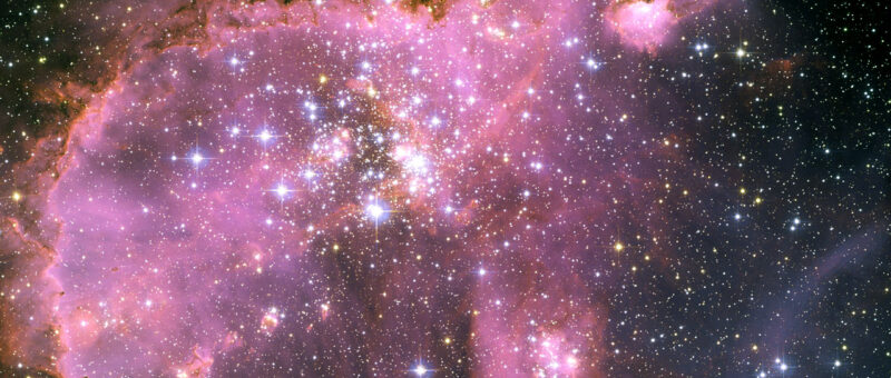 A light pink nebula filled with many bright stars.