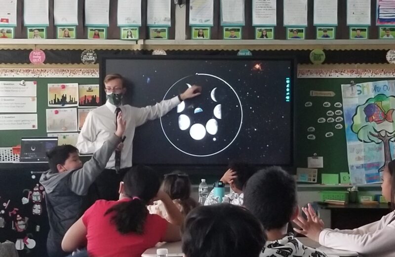 An astronomy educator shows the phases of the Moon, arranged in a ring, to students in a classroom.