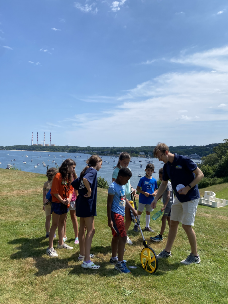 Junior Astronomers measuring distances w with an astronomy educator with Northport Bay in the background.