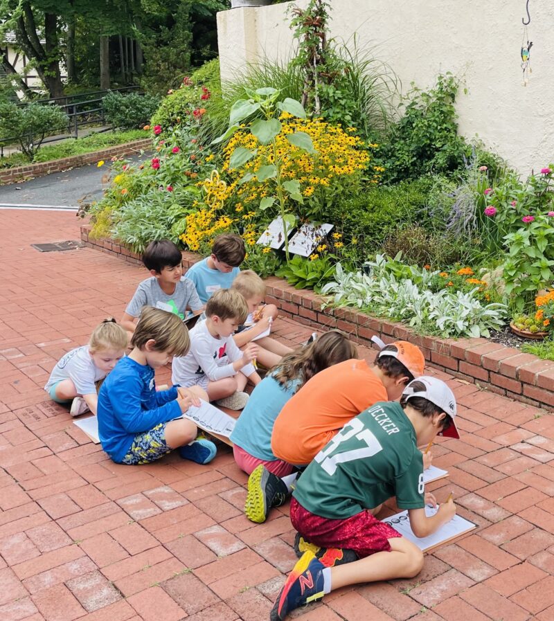 A group of Junior Explorers draw on a brick path with chalk.